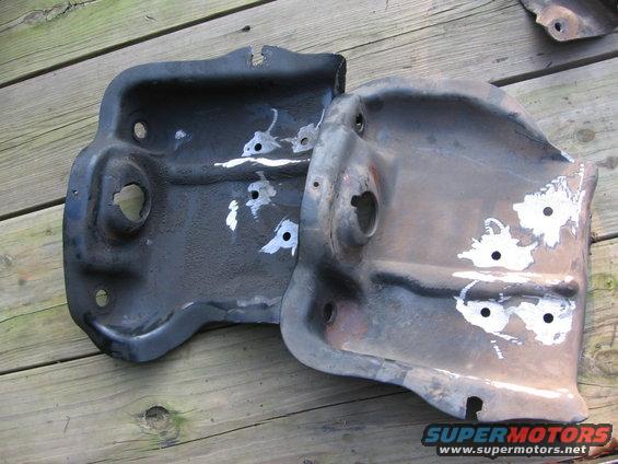 Two dark metal brackets with white paint marks and circular holes, resting on a wooden surface