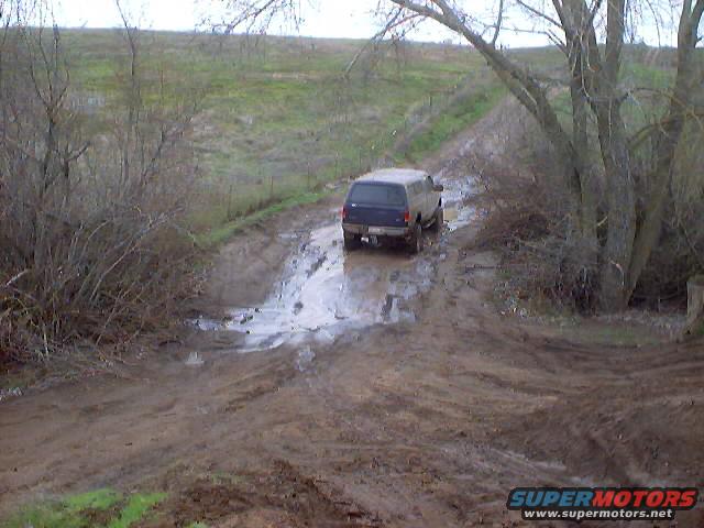 blue SUV driving on a muddy, wet road with trees and brush on the sides