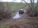 1976 Ford F-100 - A blue SUV navigates a muddy track with puddles and tire ruts.