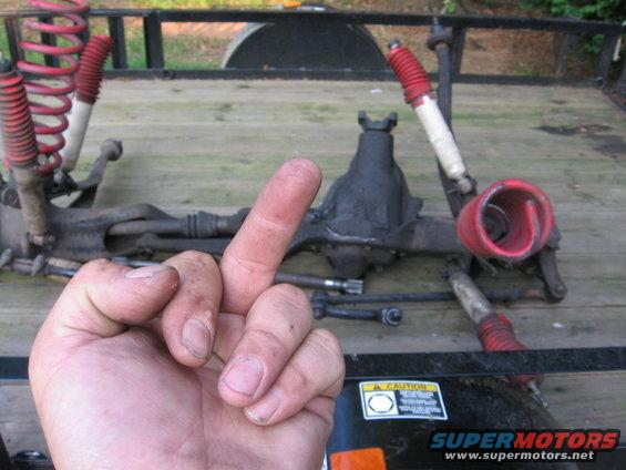 Front axle assembly with red springs and shocks, hand giving middle finger