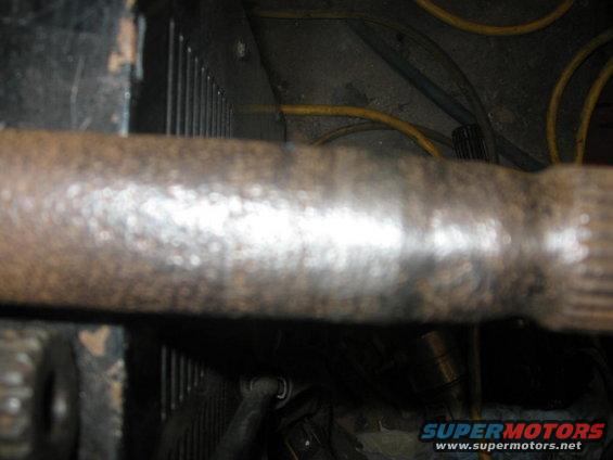 Close-up of a rusty driveshaft with some wiring in the background