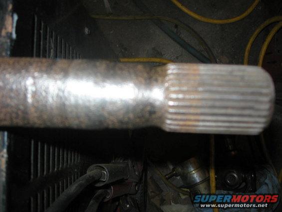 Metal shaft with splined end, showing rust and wear. Visible in a dark, cluttered area with yellow hoses
