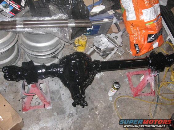 Black rear axle assembly on red jack stands with tools and supplies in background