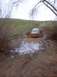 1976 Ford F-100 - A van navigates a muddy obstacle on an off-road trail, kicking up a large spray of water and mud.