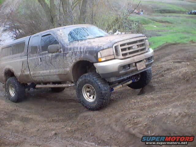 Muddy Ford Super Duty pickup truck with a camper shell, lifted with large tires, driving on a dirt track