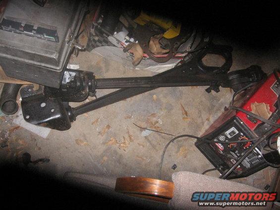 Black automotive suspension components and a red battery charger on a concrete floor