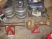 1988 Ford Bronco - A rusty rear axle assembly is supported by jack stands, with spare wheels and a cooler nearby.