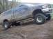 1976 Ford F-100 - A four-door pickup truck covered in mud navigates a muddy incline.