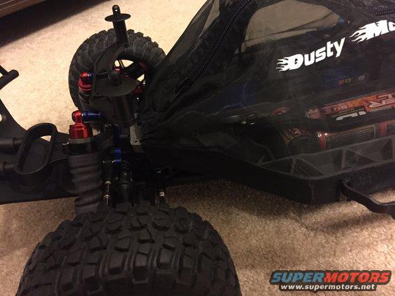 RC car chassis with suspension and knobby tires next to a black bag with 'Dusty Motors' logo