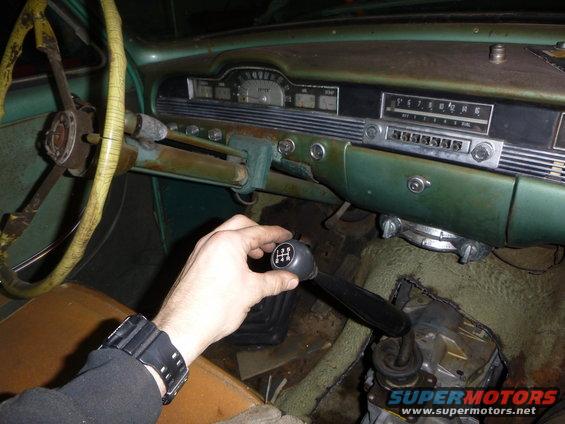Hand shifting a manual transmission in a vintage car interior. Dashboard has radio and gauges