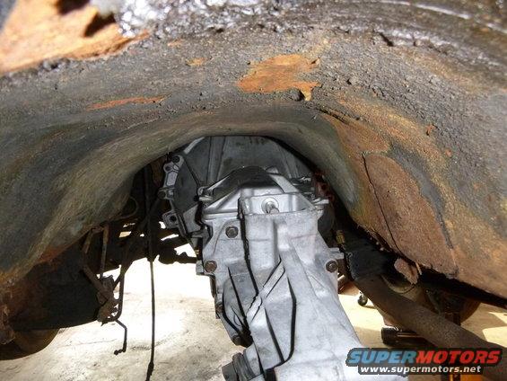 Underside view of a vehicle's transmission and rusty wheel well