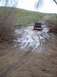 1976 Ford F-100 - A black pickup truck navigates a challenging muddy track with puddles and tire ruts.