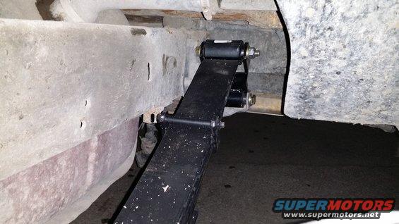 Close-up of a leaf spring attached to a vehicle frame with new bushings