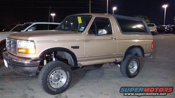 Tan 1996 Ford Bronco with aftermarket wheels and tires, lifted suspension, parked at night
