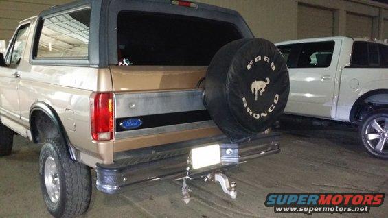 Rear view of a tan 1996 Ford Bronco with a spare tire cover. White pickup truck parked nearby