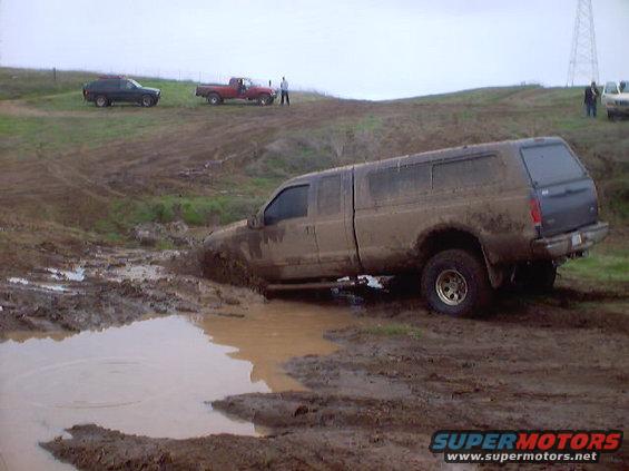 Mud-covered pickup truck stuck in a muddy field with other vehicles in the background