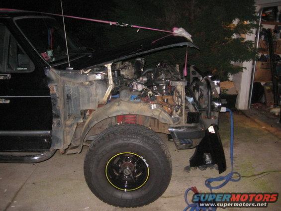 Truck with hood up, engine compartment visible. Front fender removed, showing suspension and tire