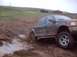 1976 Ford F-100 - Pickup truck navigates a challenging muddy terrain, with other vehicles and individuals in the distance.