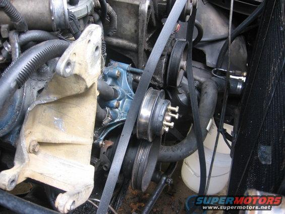 Engine bay showing belts, pulleys, and a blue pump. Some hoses and wiring are visible