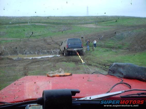 SUV stuck in mud, being pulled by another vehicle. Two people watch