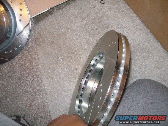 Two new slotted and drilled brake rotors, one held by a hand