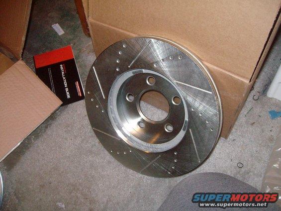 Slotted and drilled brake rotor next to an installation guide and cardboard boxes