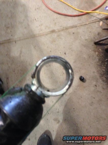 Close-up of a metal ring with a green strap attached, resting on a concrete floor