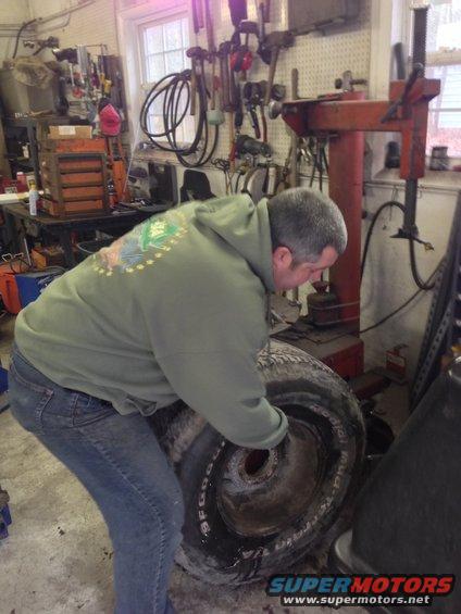 Man in a garage working on a tire. Tools and a tire machine are visible