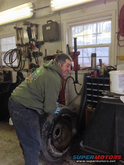 Man in green hoodie and jeans holding a tire in a garage