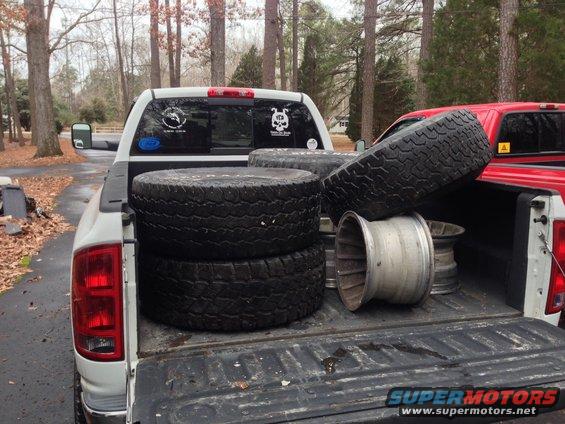 Pickup truck bed loaded with tires and rims, red truck visible