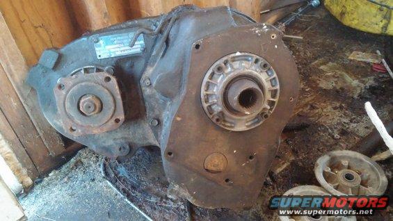 Transfer case with a blue metal tag on it. Some parts and wheels are on the floor nearby