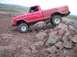 1976 Ford F-100 - A red pickup truck navigates a rocky terrain, its tires gripping the uneven surface.