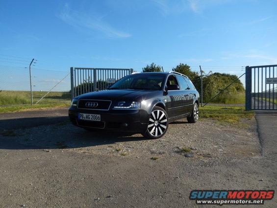 Dark gray 2003 Audi A6 Avant wagon parked on gravel lot with large metal gates in background