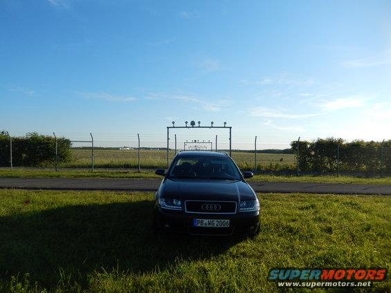 Black Audi sedan with license plate PB-WG 2006 parked in front of an airport fence