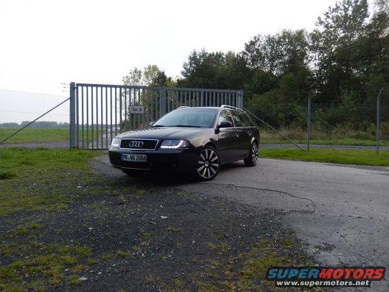Dark gray Audi A6 Avant parked in front of a metal gate, front 3/4 view