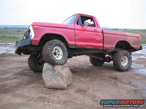 Red lifted pickup truck with large tires, front tire on a rock. Appears to be a 1977 Ford F-100