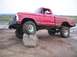 1976 Ford F-100 - A red pickup truck with off-road tires is positioned with its front tire resting on a large rock.