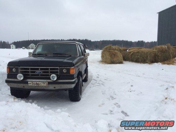 Black 1987 Ford Bronco parked in snow with hay bales and a building in the background