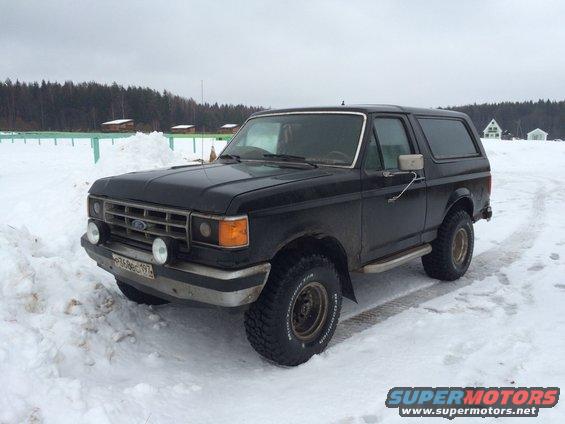 Black 1987 Ford Bronco parked in snow. Front grille and headlights visible