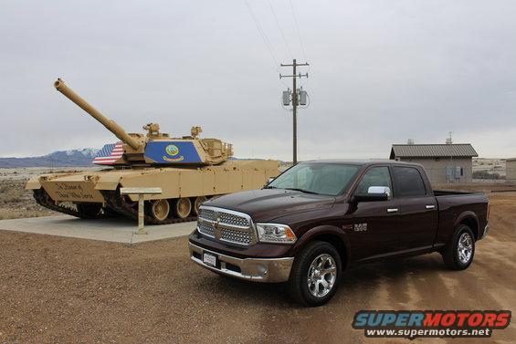 Maroon 2015 Dodge Ram 1500 parked on gravel lot with a tan military tank behind it