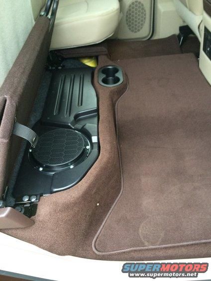 Interior shot of a vehicle's rear floor area, showing a subwoofer and cup holders