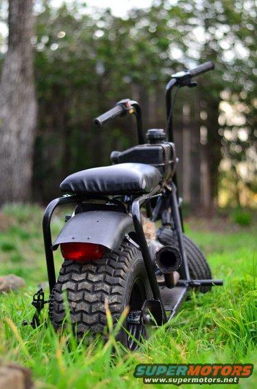 Rear view of a black mini bike with knobby tires and a red taillight, parked in grass