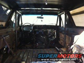 Ford Bronco interior with roll cage, stripped dashboard, and wooden floor