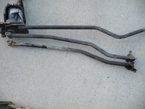 Three metal shift linkage rods and part of a shifter assembly on a concrete surface