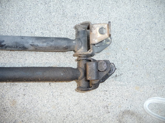 Two black car suspension rods with metal brackets attached, resting on a concrete surface
