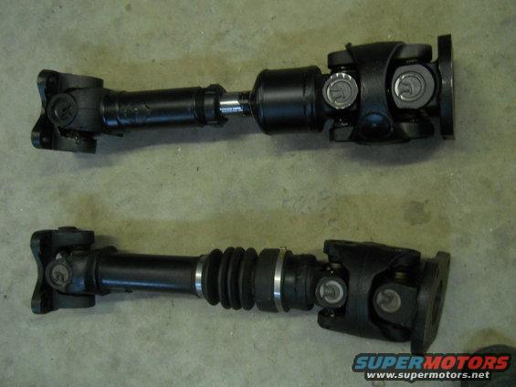 Two driveshafts, one with a rubber boot, laid out on a concrete floor