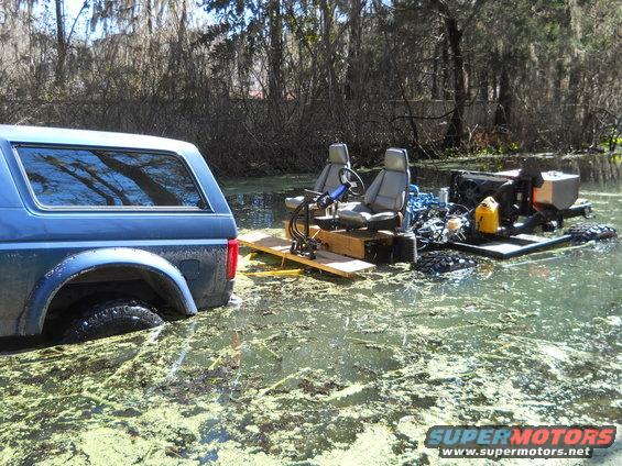 Side view of blue 1992 Ford Bronco stuck in swamp, next to homemade boat