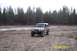 1990 Ford Bronco - A silver Jeep Wrangler sits in a dirt lot with a forest behind it.