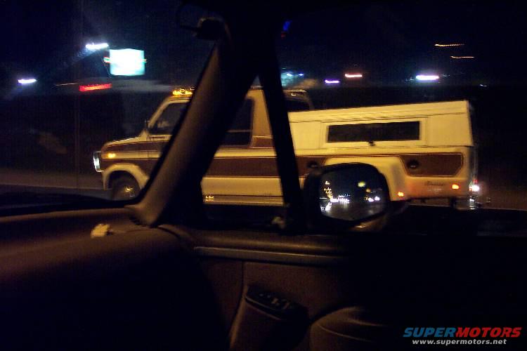 Ford pickup truck with brown stripe and white camper shell driving at night
