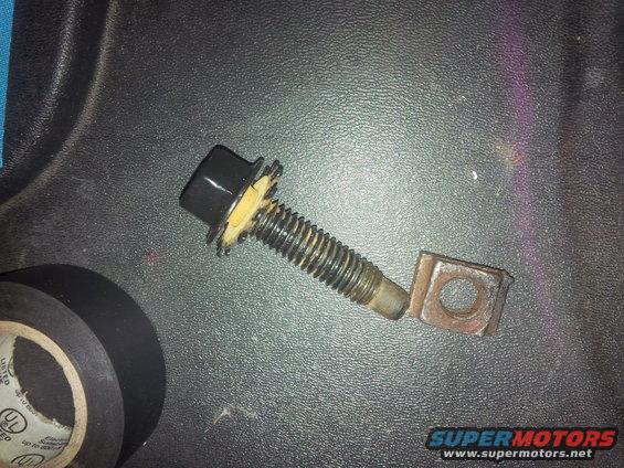 Bolt with black cap and serrated washer next to a square nut on a textured surface, with electrical tape in the corner